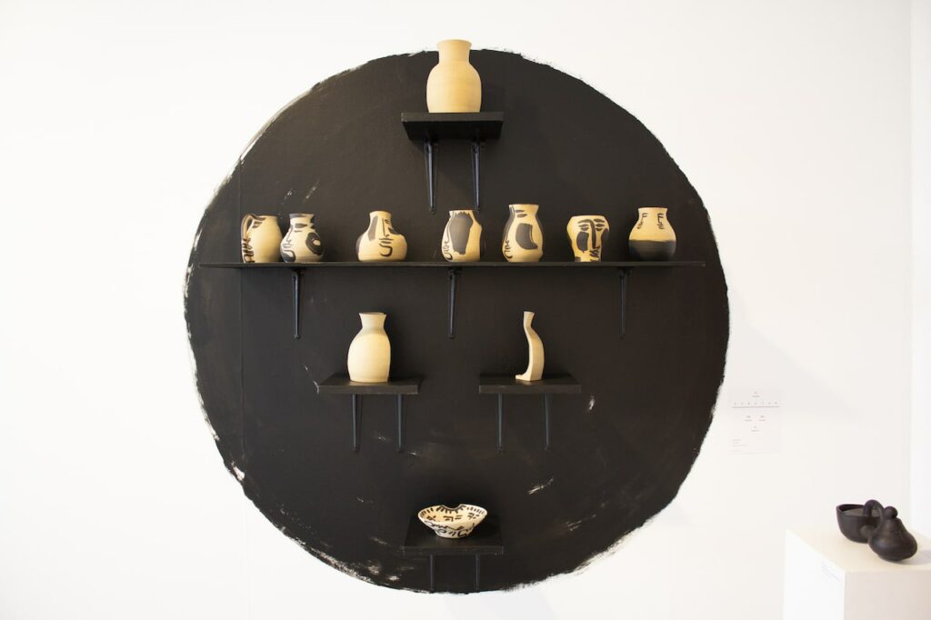 white pots on gallery wall, on black shelves in front of black circle painted on wall