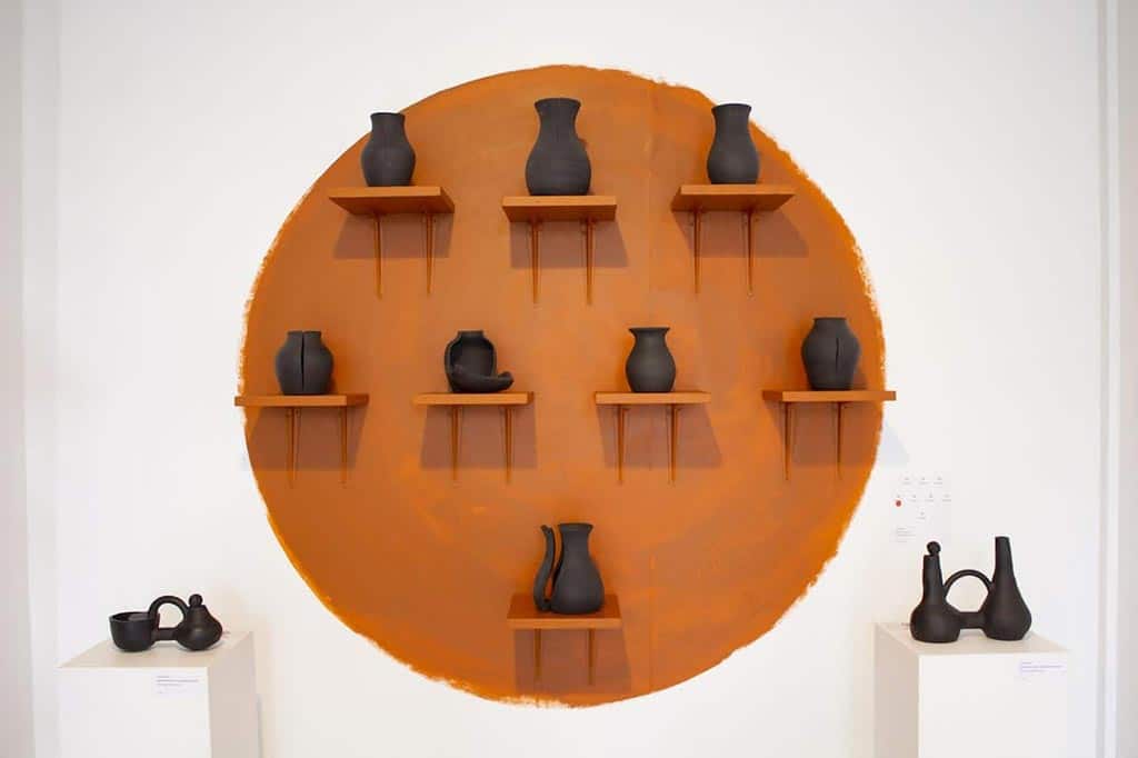 black pots on gallery wall, on orange shelves in front of orange circle painted on wall