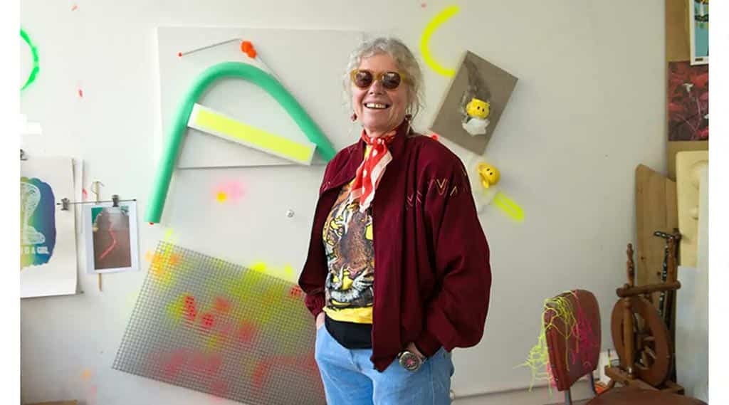 Photo of artist Judy Darragh in front of artworks in studio