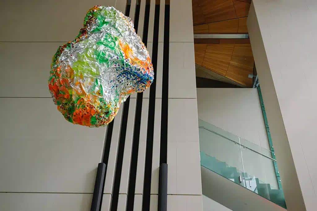 organic, rock shaped colourful sculpture hanging from ceiling in stairwell of commercial building.