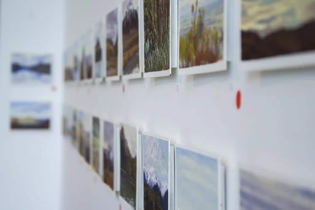 landscape paintings hanging on wall with some sold stickers