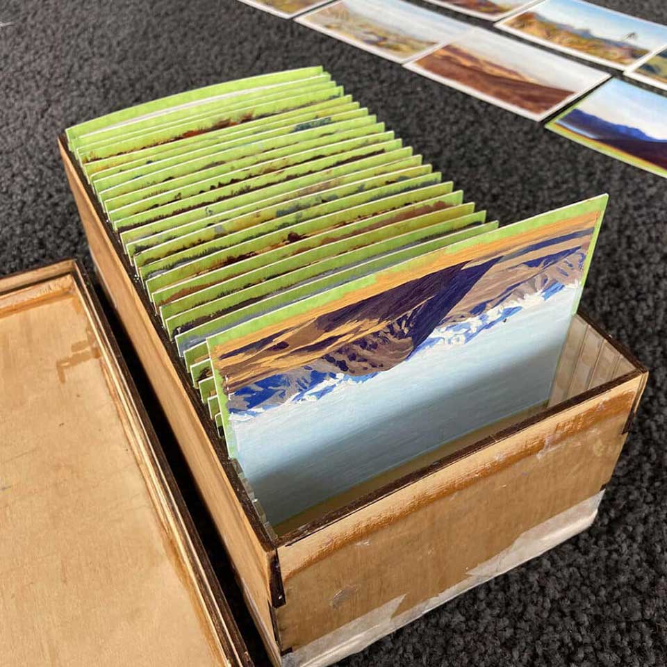 Box with landscape paintings in it, stacked in grooves like records